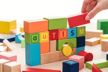 cropped view of female hand near autism lettering made of colorful building blocks on wooden surface isolated on white clipart
