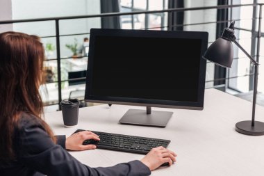 cropped view of woman using computer at workplace with lamp and coffee to go in modern office clipart