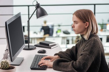 sad girl sitting at workplace and typing on computer keyboard in modern office clipart