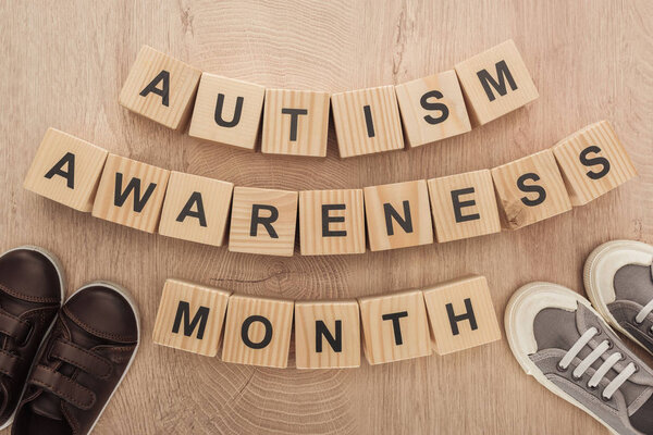 top view of autism awareness month words made of wooden blocks near brown and grey children sneakers