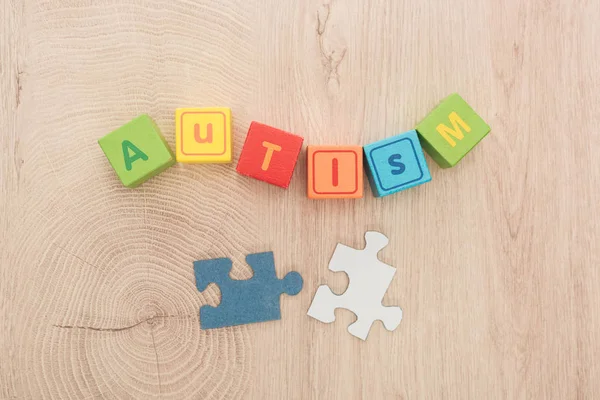 top view of autism lettering made of multicolored cubes near puzzle pieces on wooden table