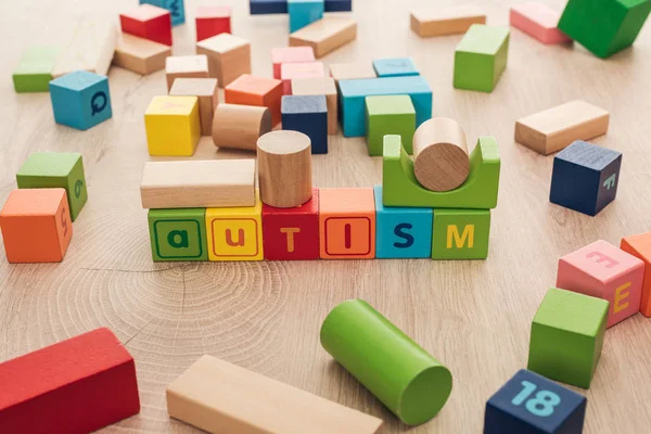 autism lettering made of multicolored cubes among building blocks on wooden surface