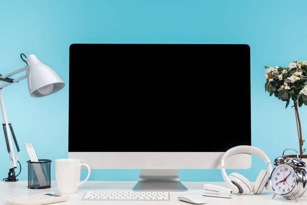workplace with computer, lamp, stationery and headphones on white table on blue background