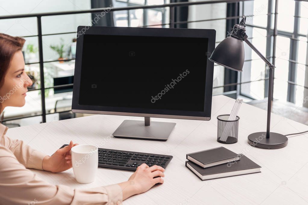 selective focus of woman sitting with cup near computer at workplace in office