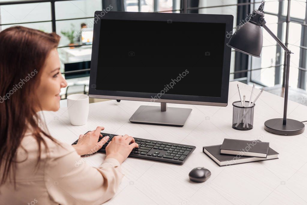 selective focus of smiling woman using computer at workplace 