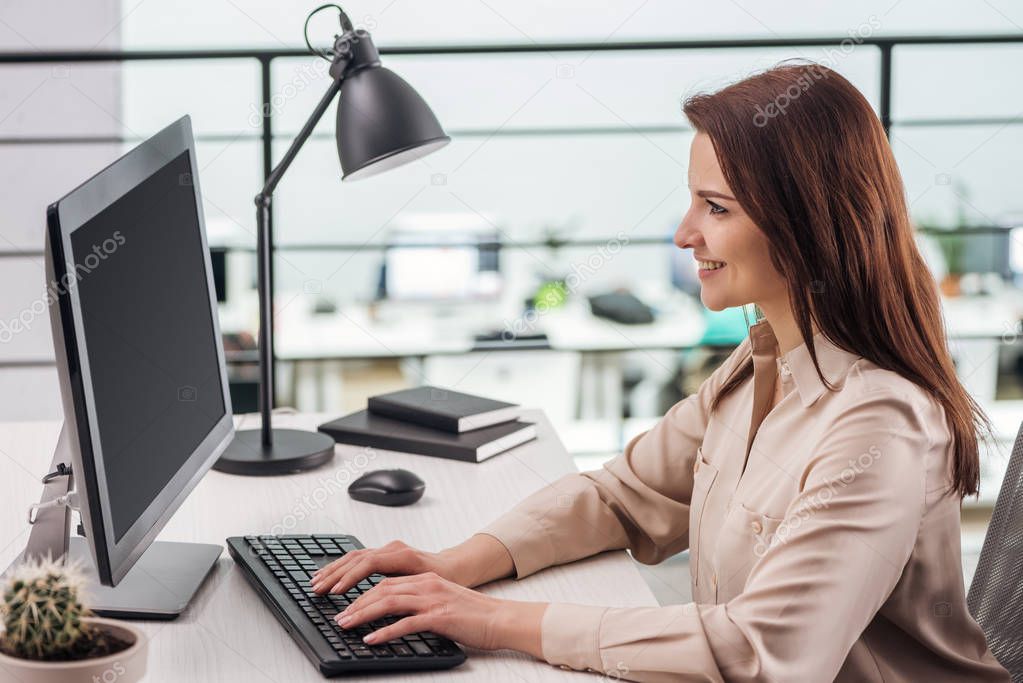 smiling young woman typing on computer keyboard at workplace in modern office