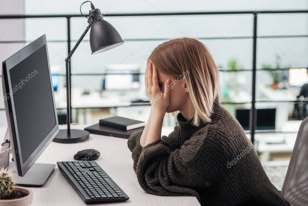 upset girl sitting at workplace with hands on face in modern office