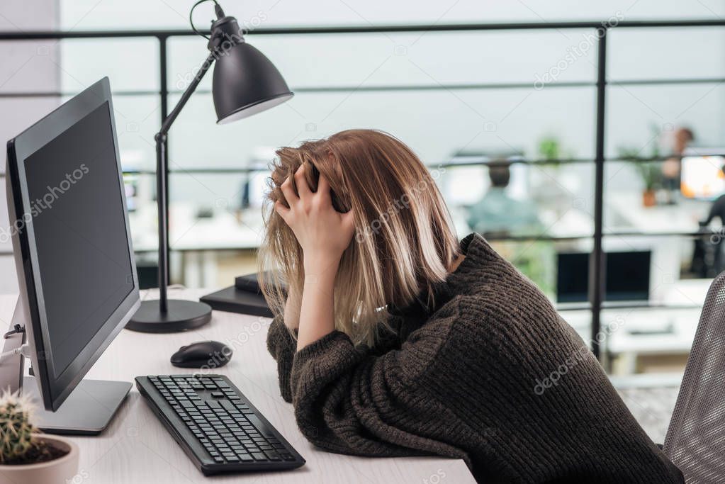 depressed girl sitting at workplace with hands on head in modern office