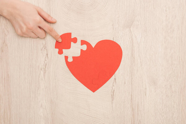 partial view of woman pointing with finger to puzzle of heart 