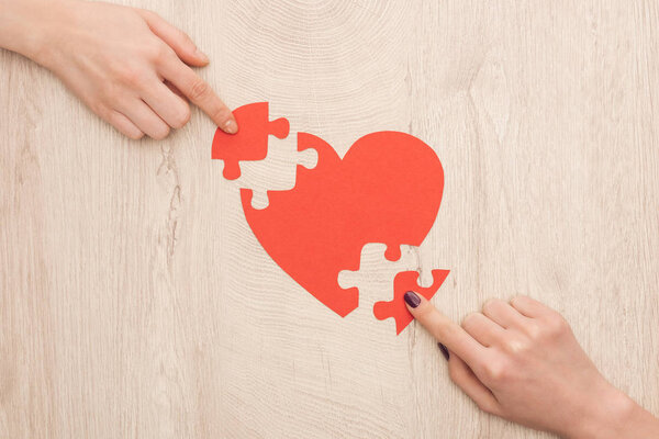 cropped view of women pointing with fingers to pieces of puzzle and paper heart 