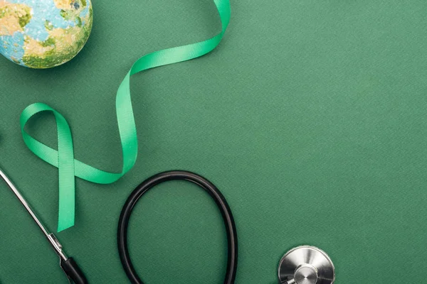 top view of green ribbon, toy earth and stethoscope on green background