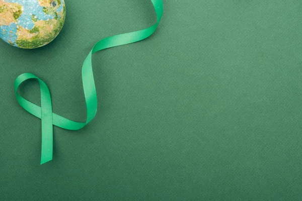 top view of green ribbon and toy earth on green background with copy space