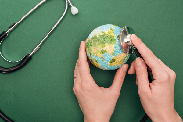 partial view of woman holding toy earth and stethoscope on green background 
