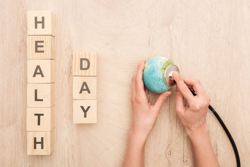 Partial view of woman holding stethoscope, toy heart and cubes with health day lettering
