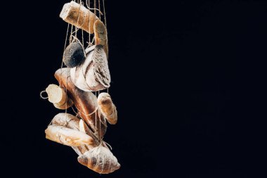 fresh baked bread, baguettes and croissant with flour hanging on ropes isolated on black with copy space clipart