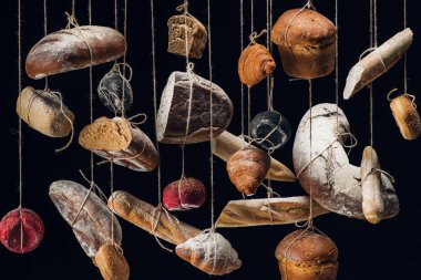 loaves of white and brown bread and pastry hanging on ropes isolated on black clipart