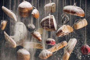 Beyaz ve kahverengi ekmek ve pasta halatlar üzerinde asılı somun, düşen beyaz un 