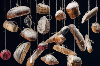 white and brown bread and pastry hanging on ropes isolated on black clipart
