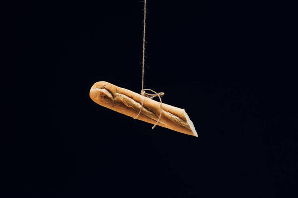 cut fresh baked baguette hanging on rope isolated on black