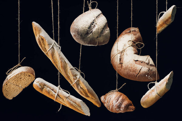 fresh baked bread, baguettes and croissant with flour hanging on ropes isolated on black