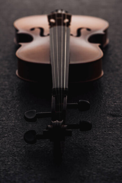 close up of strings on cello in darkness on grey textured surface 