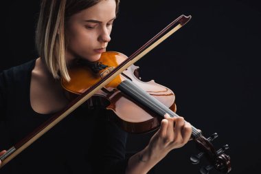 young concentrated woman playing cello with bow isolated on black clipart