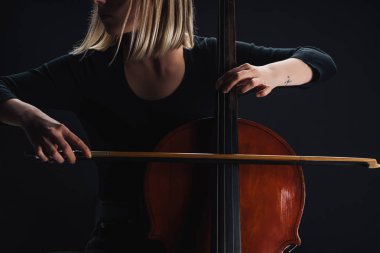 cropped view of young woman playing double bass in darkness isolated on black clipart