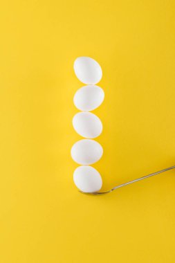 sarı arka planda kaşık üzerinde beş beyaz tavuk yumurtası