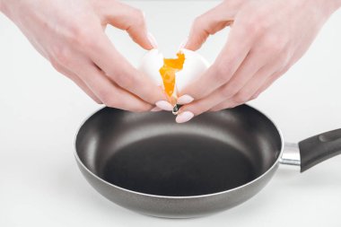cropped view of woman smashing egg with hands into pan on white background clipart