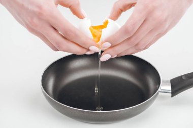 partial view of woman smashing egg with hands into pan on white background clipart