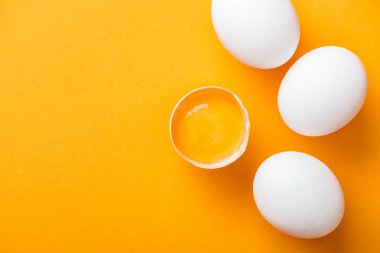top view of smashed chicken egg with yolk on bright orange background among white whole eggs clipart