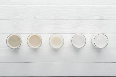top view of different types of milk on white wooden surface clipart