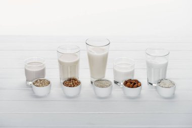 glasses with coconut, chickpea, oat, rice and almond milk on white wooden table with ingredients in bowls isolated on white clipart