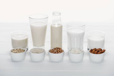 beyaz üzerinde izole kase malzemelerle Beyaz ahşap masa üzerinde Hindistan cevizi, nohut, yulaf, pirinç ve badem sütü ile gözlük ve şişe