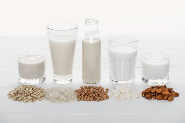 beyaz üzerinde izole maddeler ile beyaz ahşap yüzey üzerinde Hindistan cevizi, nohut, yulaf, pirinç ve badem sütü ile gözlük ve şişe