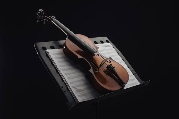 classic wooden cello on opened music book on stand isolated on black 