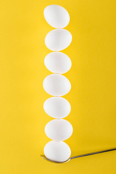 seven white chicken eggs on spoon on yellow background