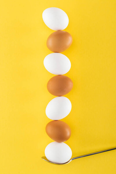 seven white and brown chicken eggs on spoon on yellow background