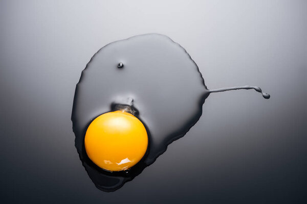 close up of raw smashed egg with yolk and protein on black background