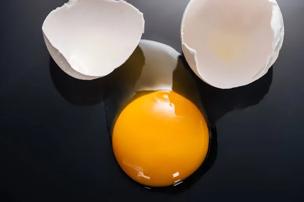 黒の背景に卵黄 タンパク質と卵殻と生の強打の卵のクローズアップ — ストック写真
