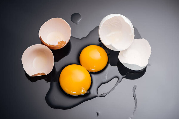 top view of raw smashed chicken eggs with yolks, proteins and eggshell on black background