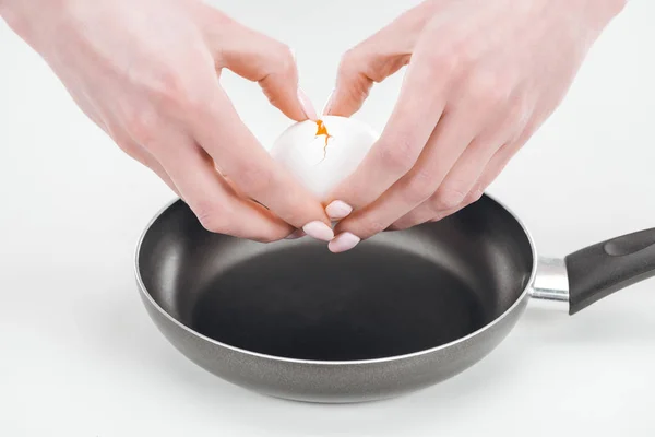 cropped view of woman smashing egg into pan on white background