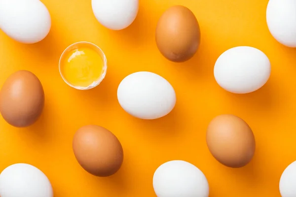 顶部的整个白色和棕色新鲜鸡蛋的顶部视图与粉碎的一个在明亮的橙色背景 — 图库照片