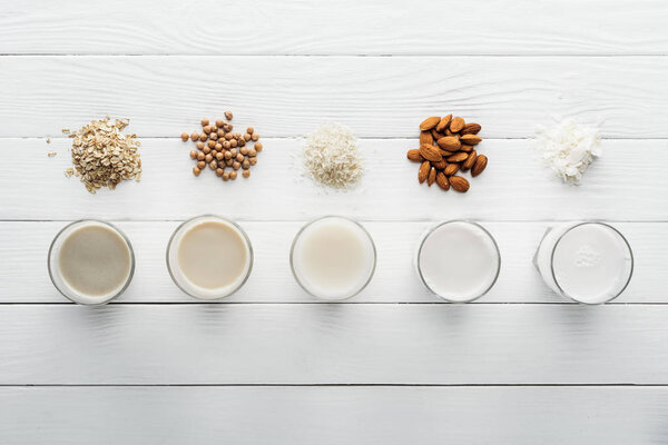 top view of glasses with coconut, chickpea, oat, rice and almond milk on wooden surface with ingredients