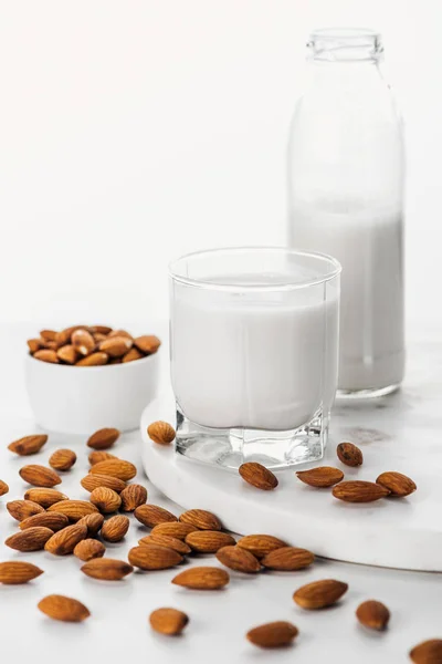 ビーガンの新鮮なアーモンドミルクをボトルに入れ ガラスのナッツの近くに白に分離されたボウル — ストック写真
