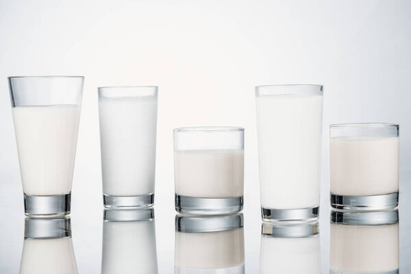 row of glasses with organic fresh vegan milk on grey background with reflection