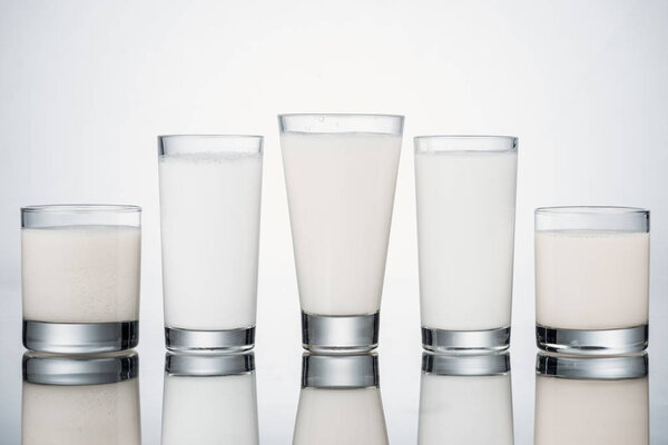 row of glasses with organic fresh alternative milk on grey background with reflection