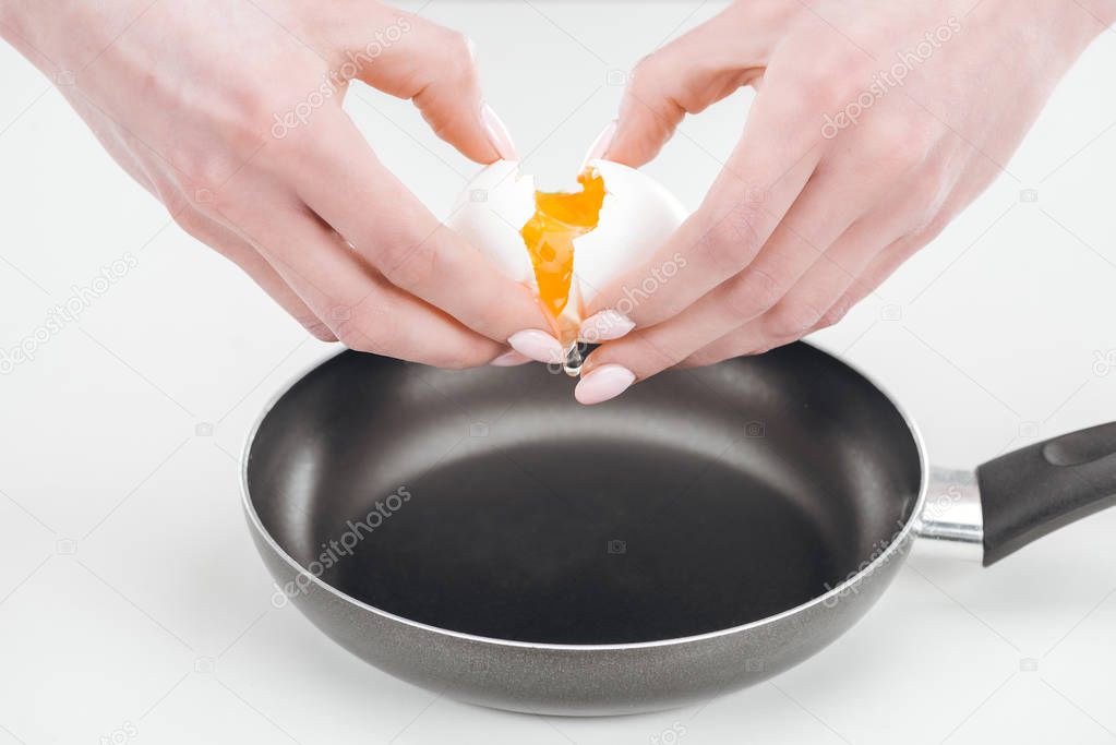 cropped view of woman smashing egg with hands into pan on white background