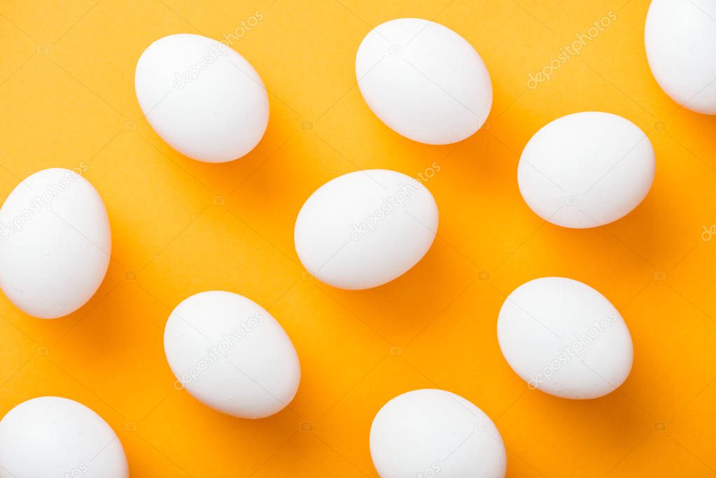 top view of whole white fresh chicken eggs on bright orange background 