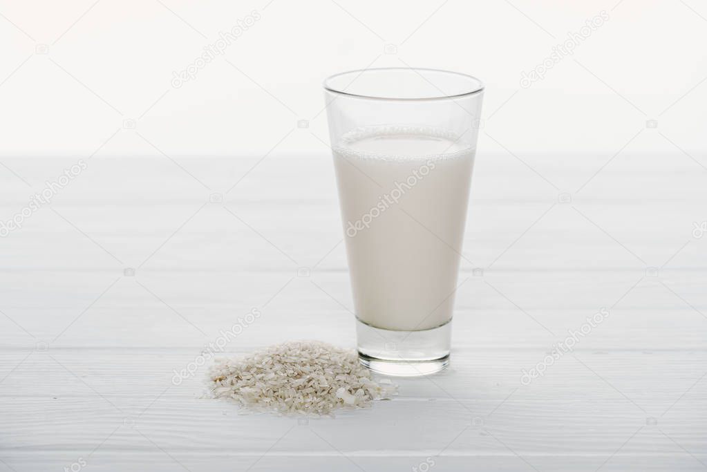rice milk in glass near rice grains on wooden table isolated on white